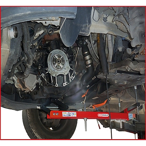 Unteransicht eines Autos. Eine Hebebühne hält den Motor. Teile des Motors sind zu sehen, darunter ein Rad und Rohre.